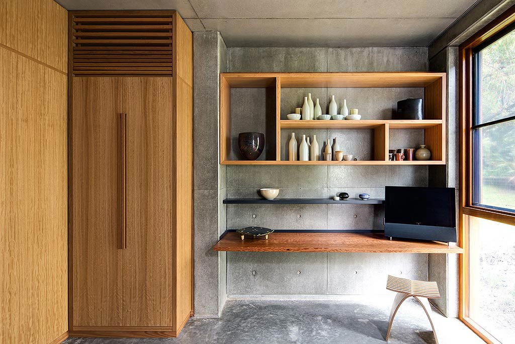 Minimalist room with a wooden cabinet, wall shelves displaying ceramics, a wooden desk with a monitor, and a modern stool.