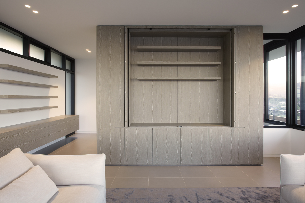 Modern living room with floor-to-ceiling wooden shelving, minimalistic decor, and large windows overlooking a cityscape.