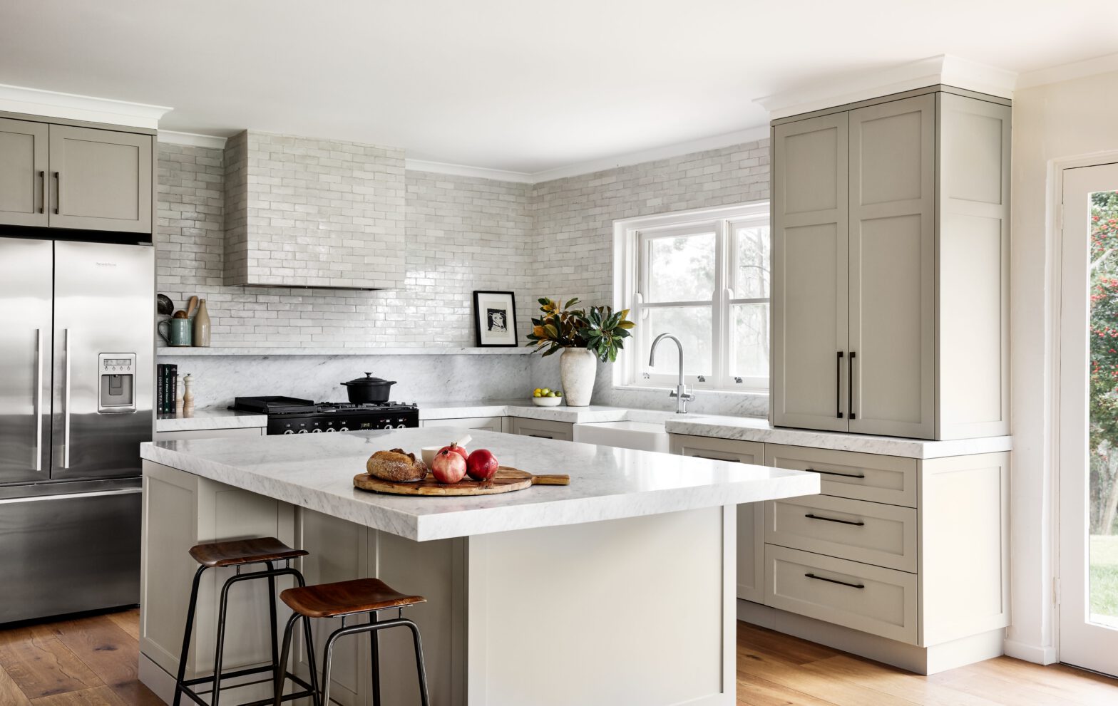Modern kitchen with marble countertops, light grey cabinets, stainless steel fridge, and a center island with bar stools.