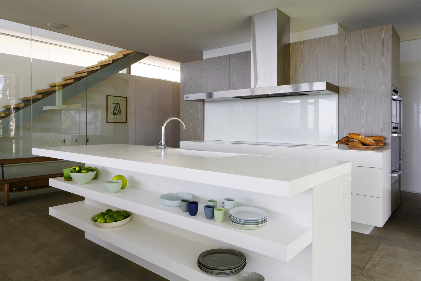 Modern kitchen with a white island, open shelves holding dishes and green apples, and stainless steel appliances.