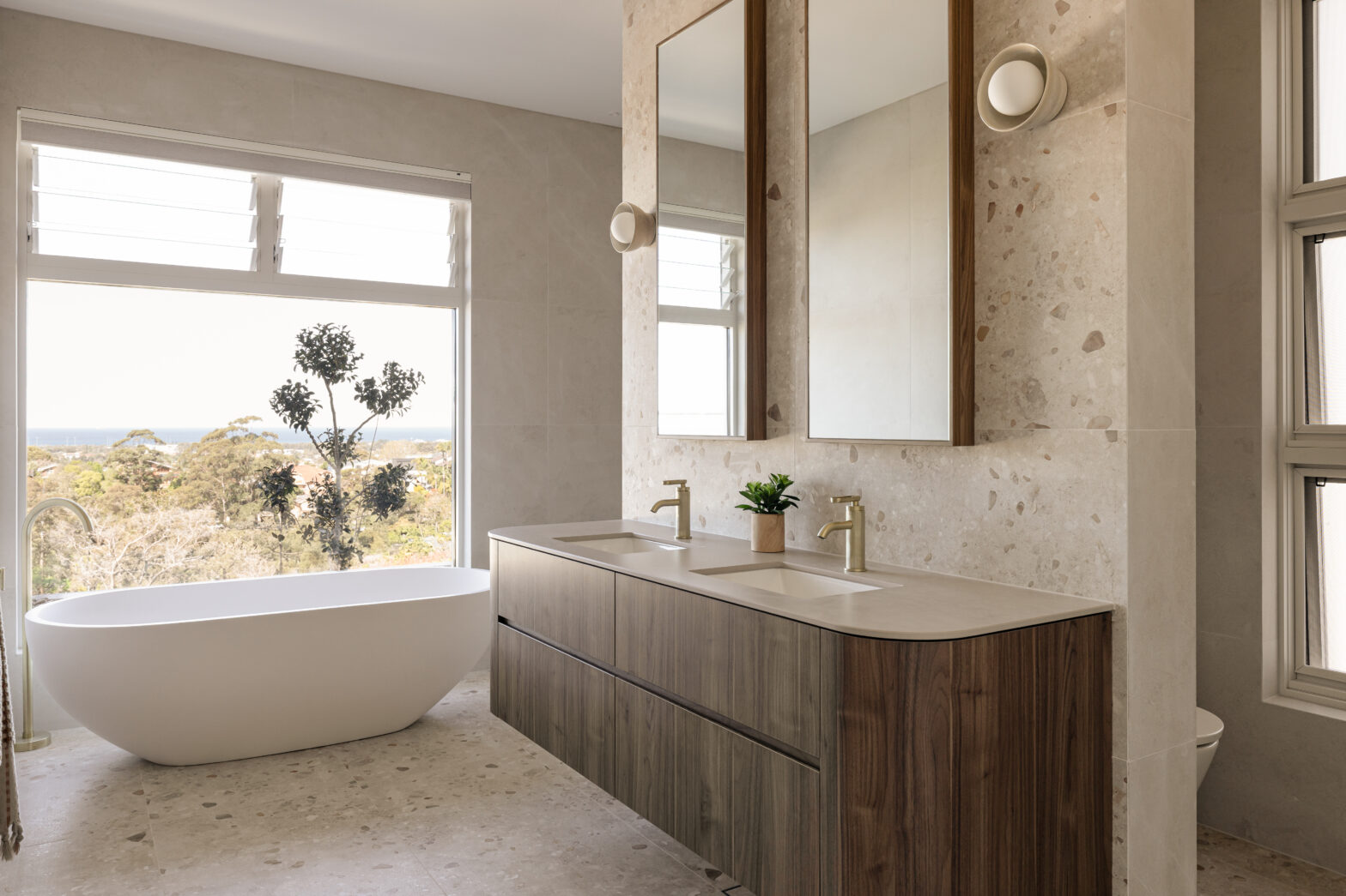 Modern bathroom with a freestanding tub, double vanity with mirrors, and large window revealing a scenic view.